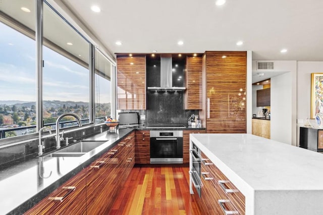 kitchen featuring a large island, sink, hardwood / wood-style floors, oven, and wall chimney exhaust hood