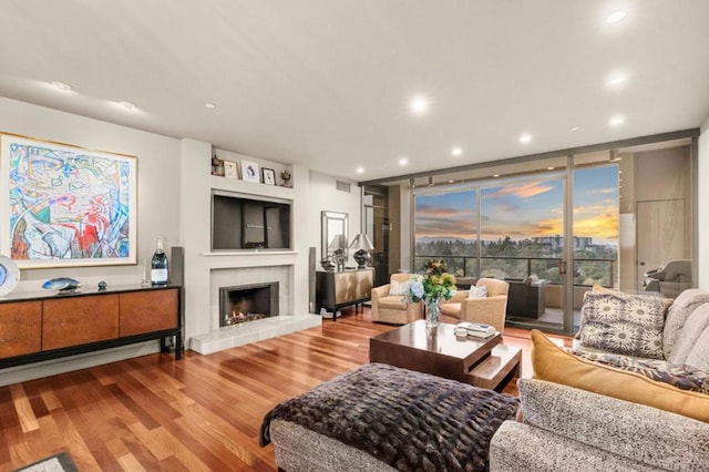 living room featuring a tile fireplace, wood-type flooring, and a wall of windows