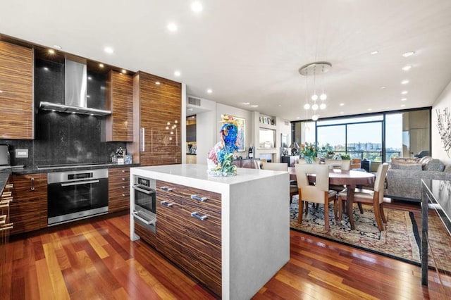 kitchen with wall chimney range hood, dark hardwood / wood-style floors, a center island, tasteful backsplash, and oven