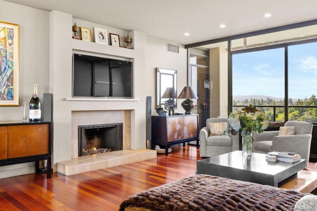 living room with a tile fireplace, wood-type flooring, and floor to ceiling windows