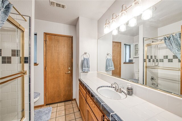 full bathroom featuring bath / shower combo with glass door, vanity, a textured ceiling, tile patterned floors, and toilet