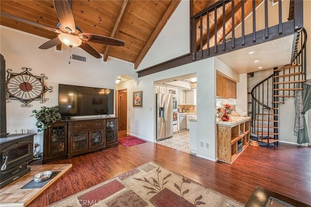 living room featuring a wood stove, hardwood / wood-style flooring, ceiling fan, wooden ceiling, and beam ceiling