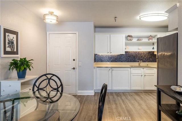 kitchen with sink, white cabinetry, black fridge, tasteful backsplash, and light hardwood / wood-style floors