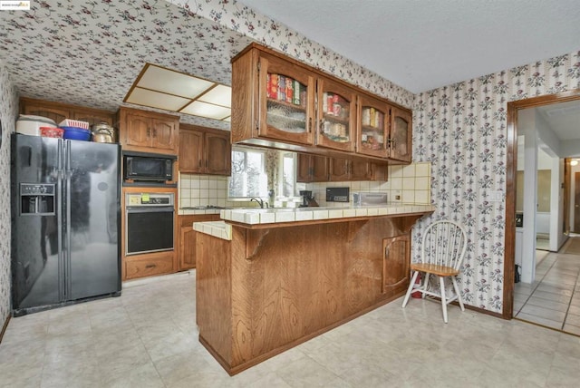 kitchen featuring decorative backsplash, tile countertops, black appliances, and kitchen peninsula