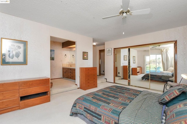 bedroom with ensuite bathroom, light carpet, a textured ceiling, and a closet