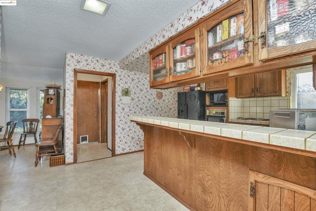 kitchen with tile counters, black appliances, and a textured ceiling