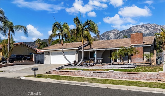 ranch-style house featuring a garage, a chimney, a mountain view, and driveway