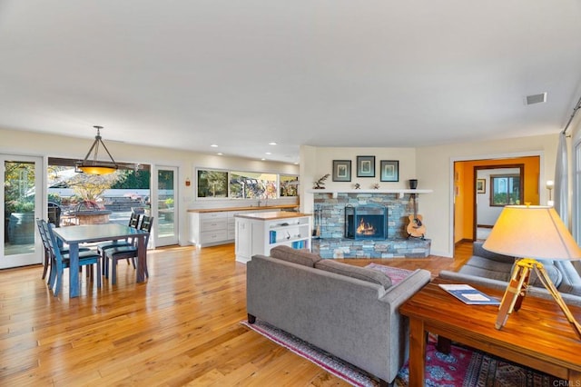 living room with a stone fireplace and light wood-type flooring