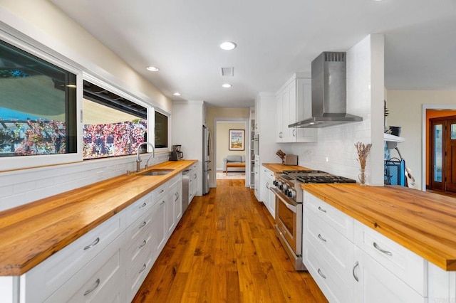 kitchen featuring stainless steel appliances, wall chimney range hood, white cabinets, and wood counters