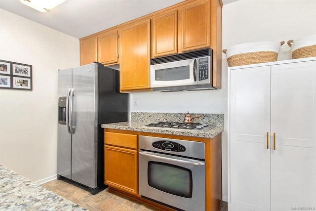 kitchen featuring appliances with stainless steel finishes, light tile patterned floors, and light stone counters