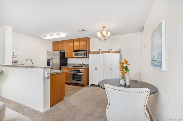 kitchen featuring decorative light fixtures, a chandelier, light carpet, kitchen peninsula, and stainless steel appliances