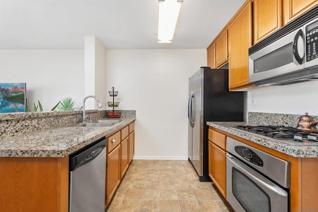 kitchen with appliances with stainless steel finishes, kitchen peninsula, sink, and light stone countertops