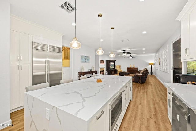 kitchen featuring built in appliances, a center island, pendant lighting, light stone countertops, and white cabinets