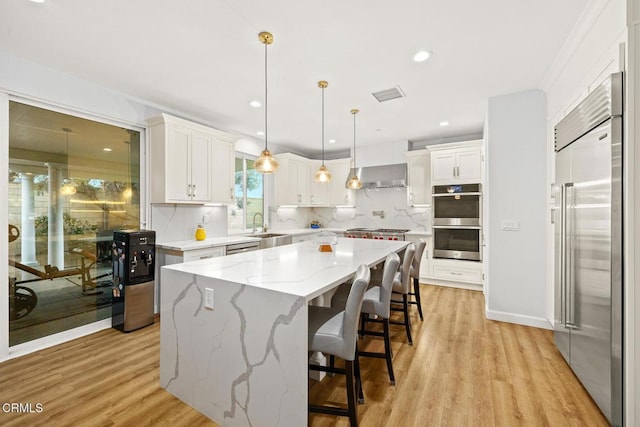 kitchen with hanging light fixtures, stainless steel appliances, white cabinets, a kitchen island, and wall chimney exhaust hood