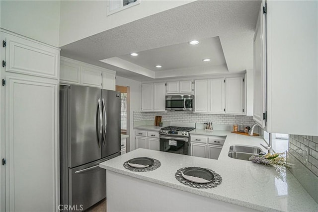 kitchen featuring appliances with stainless steel finishes, sink, white cabinets, kitchen peninsula, and a raised ceiling