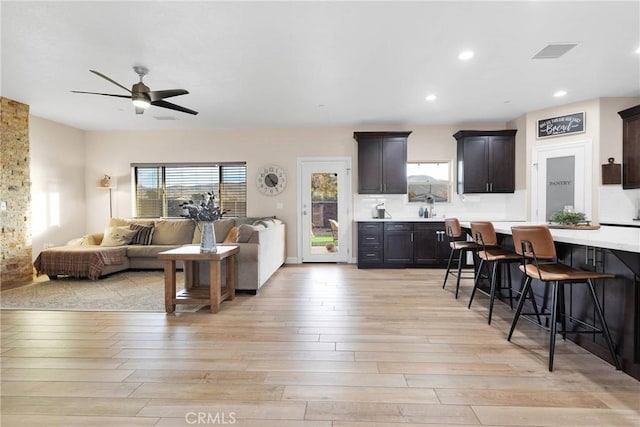 kitchen with a breakfast bar, sink, ceiling fan, dark brown cabinets, and light hardwood / wood-style flooring