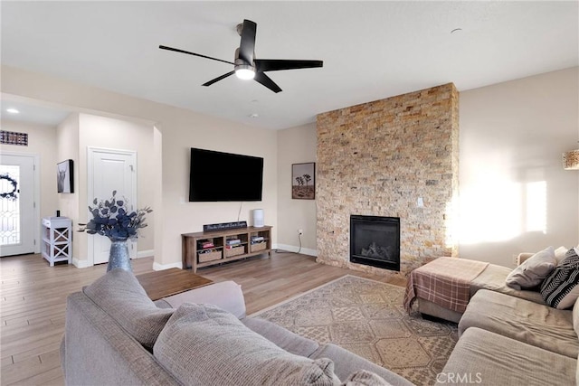 living room with wood-type flooring, plenty of natural light, a stone fireplace, and ceiling fan