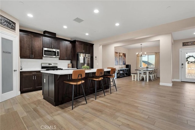 kitchen with appliances with stainless steel finishes, light wood-type flooring, a center island with sink, and a kitchen bar