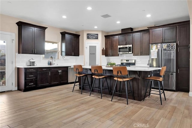 kitchen with a kitchen bar, a center island, dark brown cabinetry, light hardwood / wood-style floors, and stainless steel appliances