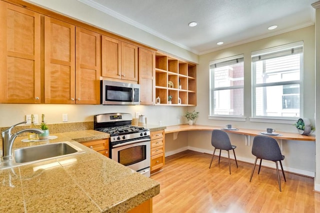 kitchen with sink, built in desk, ornamental molding, stainless steel appliances, and light hardwood / wood-style floors