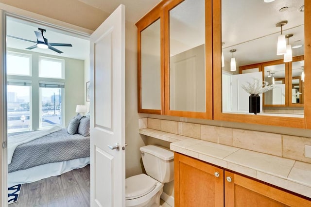 bathroom with hardwood / wood-style flooring, ceiling fan, backsplash, vanity, and toilet