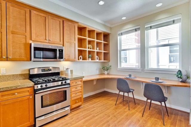 kitchen with ornamental molding, stainless steel appliances, built in desk, and light hardwood / wood-style floors