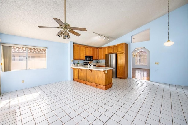 kitchen featuring brown cabinets, freestanding refrigerator, a peninsula, light countertops, and black microwave