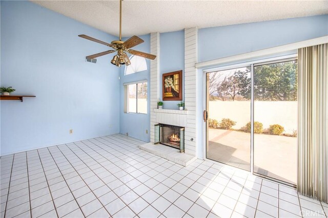 unfurnished living room featuring vaulted ceiling, a textured ceiling, light tile patterned floors, ceiling fan, and a fireplace