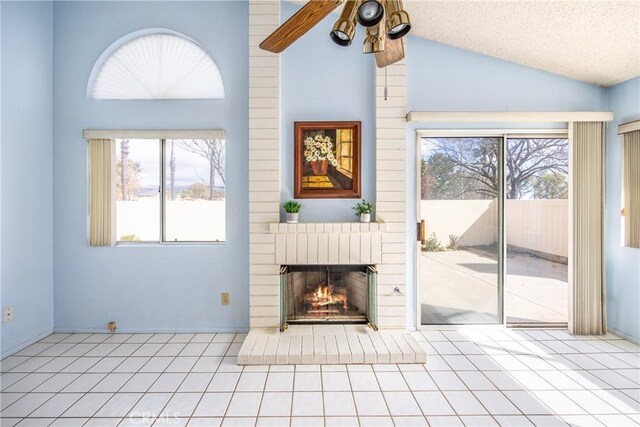 unfurnished living room with light tile patterned flooring, vaulted ceiling, a textured ceiling, ceiling fan, and a fireplace