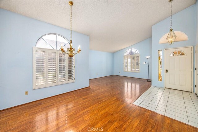 entryway with a healthy amount of sunlight, hardwood / wood-style flooring, vaulted ceiling, and a chandelier