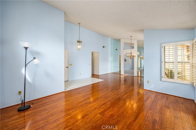 unfurnished living room with vaulted ceiling, hardwood / wood-style floors, a textured ceiling, and an inviting chandelier