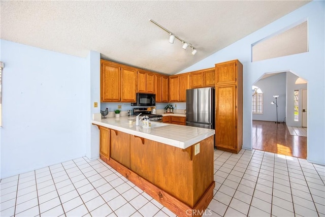 kitchen with vaulted ceiling, a textured ceiling, light tile patterned floors, appliances with stainless steel finishes, and kitchen peninsula