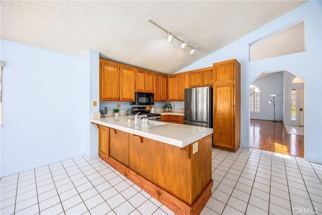 kitchen featuring arched walkways, light tile patterned floors, stainless steel appliances, light countertops, and a peninsula