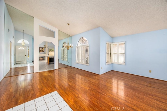 interior space featuring a warm lit fireplace, high vaulted ceiling, a textured ceiling, hardwood / wood-style flooring, and an inviting chandelier