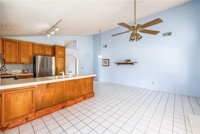 kitchen with lofted ceiling, tile countertops, stainless steel refrigerator, kitchen peninsula, and ceiling fan