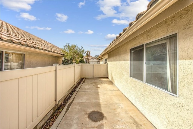 view of property exterior featuring a tile roof, fence, a patio, and stucco siding