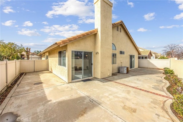 rear view of property with a patio, a tile roof, a fenced backyard, a chimney, and stucco siding