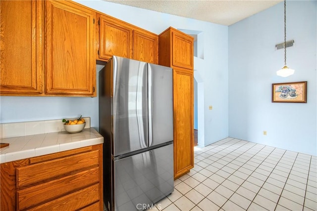 kitchen with hanging light fixtures, tile countertops, stainless steel refrigerator, and light tile patterned flooring