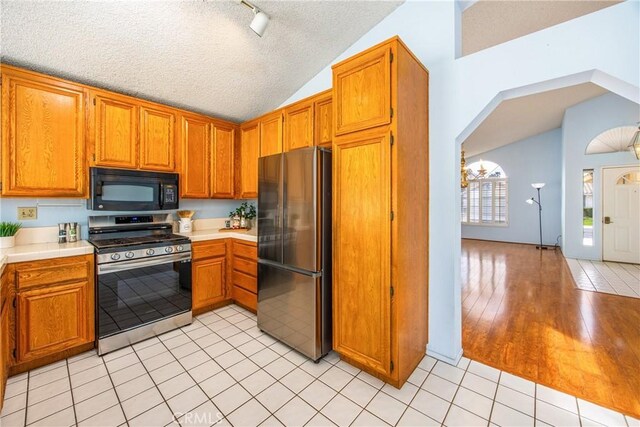 kitchen featuring lofted ceiling, stainless steel appliances, a textured ceiling, and light tile patterned flooring