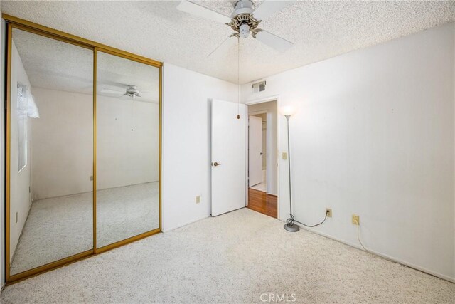 unfurnished bedroom featuring ceiling fan, light colored carpet, a closet, and a textured ceiling