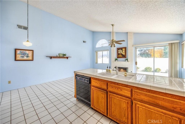 kitchen with a sink, visible vents, black dishwasher, vaulted ceiling, and a brick fireplace