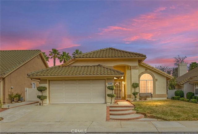 mediterranean / spanish house with driveway, a tiled roof, an attached garage, and stucco siding