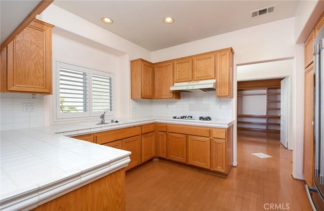 kitchen with sink, tasteful backsplash, tile countertops, light hardwood / wood-style flooring, and white gas stovetop