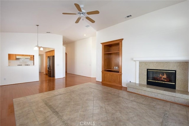 unfurnished living room with lofted ceiling, built in features, ceiling fan, a premium fireplace, and hardwood / wood-style floors