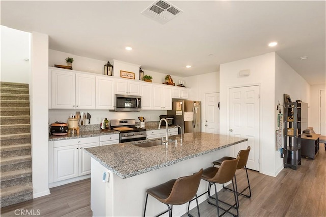 kitchen with sink, white cabinetry, stainless steel appliances, an island with sink, and stone countertops