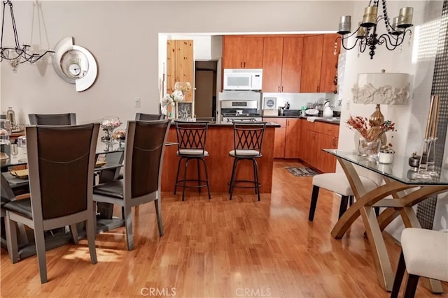 kitchen featuring a breakfast bar area, stainless steel stove, a notable chandelier, pendant lighting, and light hardwood / wood-style floors