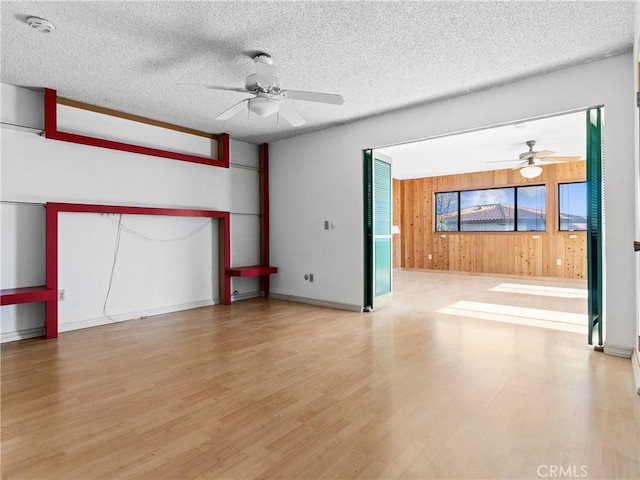 unfurnished room with ceiling fan, wood-type flooring, a textured ceiling, and wood walls