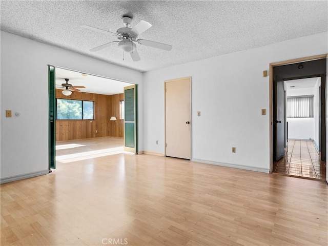 empty room featuring ceiling fan, a textured ceiling, light wood-type flooring, and wood walls