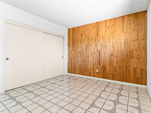 unfurnished bedroom featuring wooden walls, a closet, and a textured ceiling