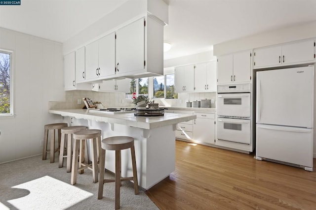 kitchen featuring white cabinetry, white appliances, a breakfast bar, and kitchen peninsula